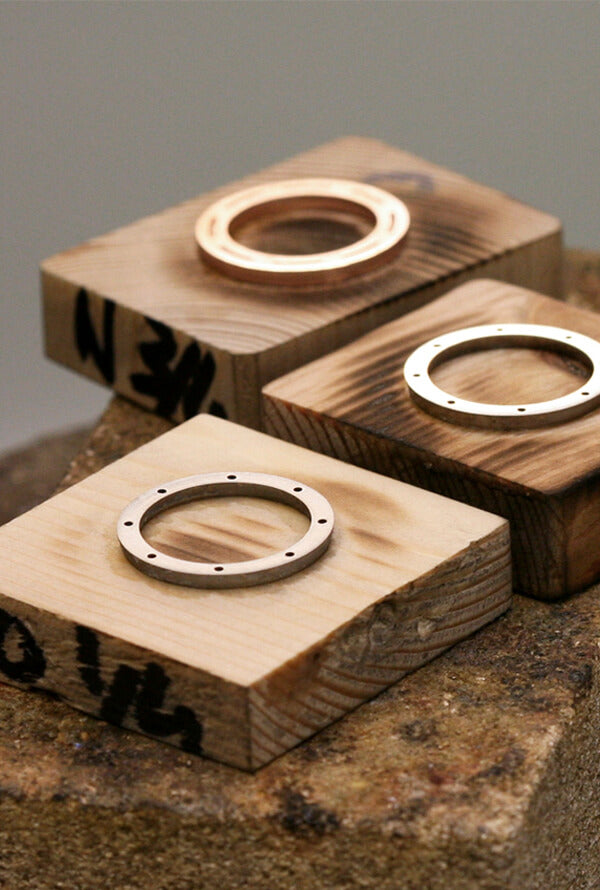 Three small wooden blocks in a jewellery workshop. On top of them are three metal rings that all make up part of the Geo ring. The wood on the wooden blocks is slightly burnt.